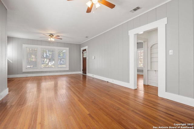 unfurnished living room featuring hardwood / wood-style flooring, ornamental molding, built in features, and ceiling fan