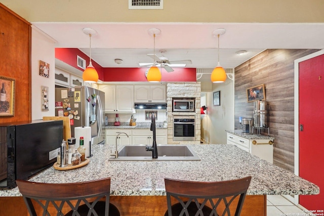 kitchen with white cabinetry, wood walls, stainless steel appliances, pendant lighting, and a breakfast bar