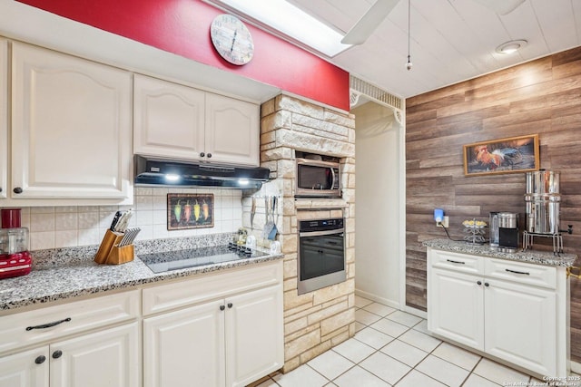 kitchen with stainless steel microwave, backsplash, black electric stovetop, oven, and light tile patterned floors