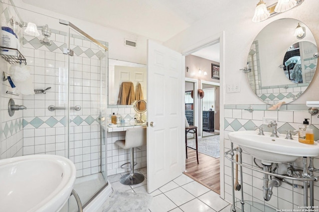 bathroom with tile patterned flooring, tile walls, a shower with door, and sink