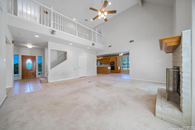 unfurnished living room featuring ceiling fan, high vaulted ceiling, a brick fireplace, and light colored carpet