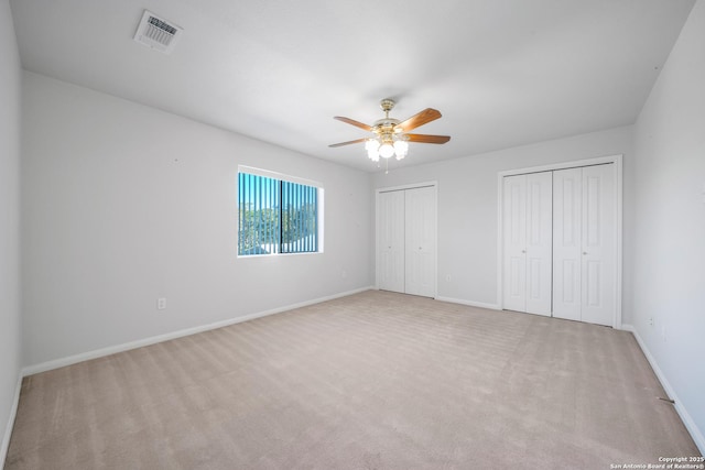 unfurnished bedroom with ceiling fan, two closets, and light carpet