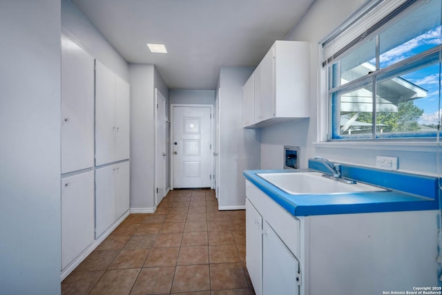 kitchen with light tile patterned floors, white cabinets, and sink