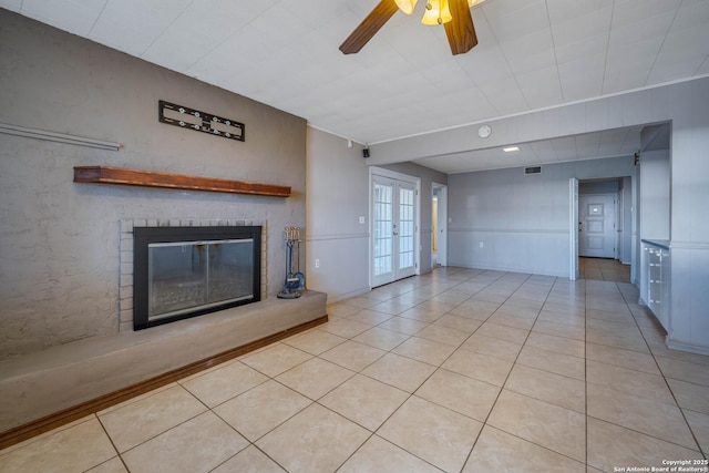 unfurnished living room with ceiling fan, light tile patterned floors, french doors, and a brick fireplace