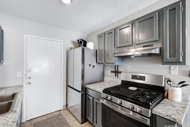 kitchen with light tile patterned floors, appliances with stainless steel finishes, light stone counters, and a textured ceiling