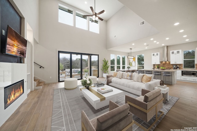 living room featuring ceiling fan, light hardwood / wood-style floors, and a towering ceiling