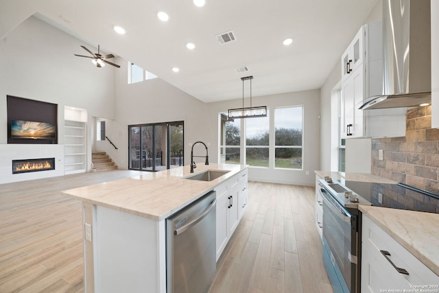 kitchen featuring white cabinetry, wall chimney range hood, stainless steel appliances, an island with sink, and sink