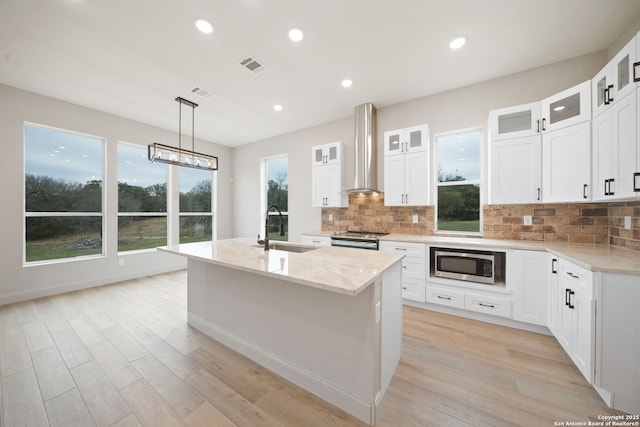 kitchen featuring wall chimney exhaust hood, white cabinetry, stainless steel appliances, sink, and a kitchen island with sink