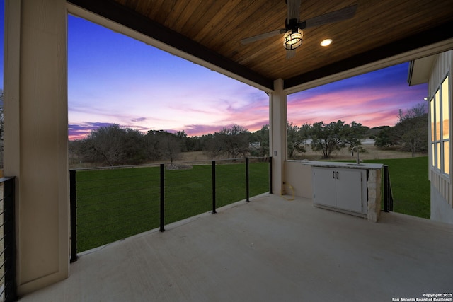 patio terrace at dusk with ceiling fan, sink, and a yard