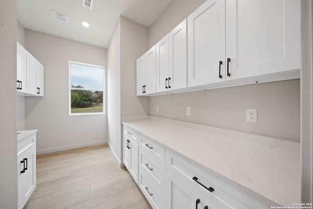 kitchen featuring white cabinetry, light hardwood / wood-style flooring, and light stone countertops