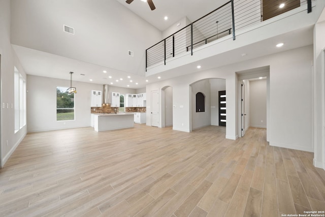 unfurnished living room featuring ceiling fan, a towering ceiling, and light hardwood / wood-style flooring