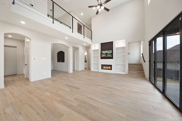 unfurnished living room with ceiling fan, built in features, and a towering ceiling