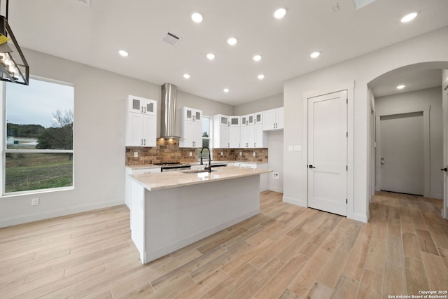 kitchen with white cabinetry, sink, a center island with sink, and wall chimney range hood