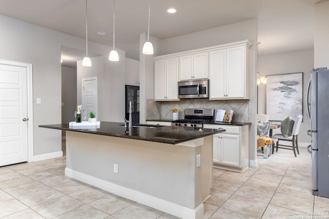 kitchen featuring white cabinets, stainless steel appliances, dark stone counters, decorative backsplash, and a center island with sink