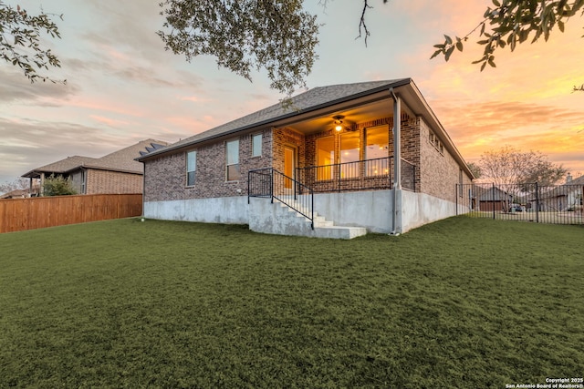 back house at dusk featuring ceiling fan and a lawn