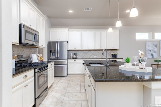 kitchen featuring appliances with stainless steel finishes, white cabinetry, decorative backsplash, sink, and a center island with sink