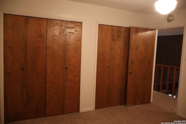 unfurnished bedroom featuring carpet, multiple closets, and a textured ceiling