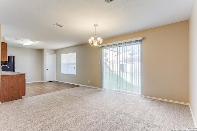 unfurnished living room with sink, light carpet, and a notable chandelier