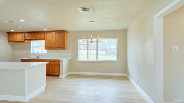 kitchen featuring pendant lighting, a healthy amount of sunlight, decorative backsplash, sink, and an inviting chandelier