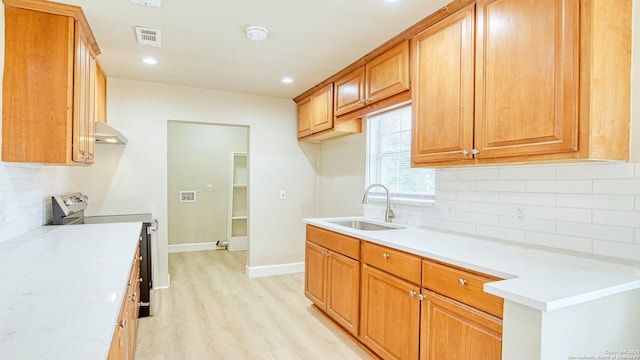 kitchen with backsplash, electric stove, light wood-type flooring, light stone countertops, and sink