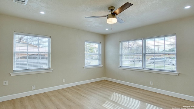 empty room featuring light wood-type flooring, ceiling fan, a healthy amount of sunlight, and a textured ceiling