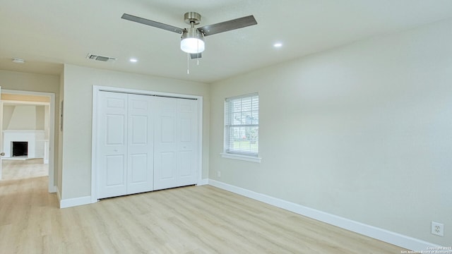 unfurnished bedroom with ceiling fan, a closet, a brick fireplace, and light wood-type flooring