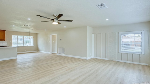 unfurnished living room featuring light wood-type flooring, ceiling fan with notable chandelier, and a textured ceiling