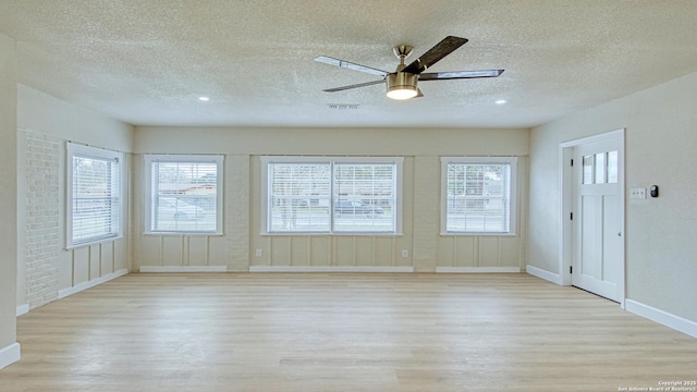 unfurnished room featuring ceiling fan, a healthy amount of sunlight, light wood-type flooring, and a textured ceiling