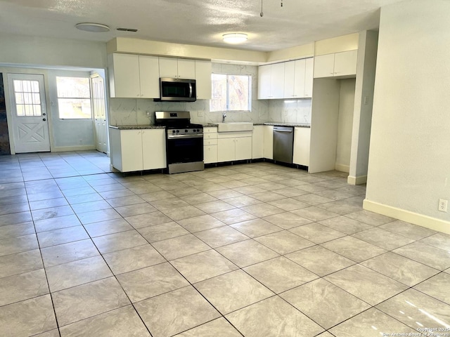 kitchen with stainless steel appliances, light tile patterned flooring, a textured ceiling, white cabinets, and sink