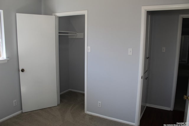 unfurnished bedroom featuring a walk in closet, a closet, and dark colored carpet