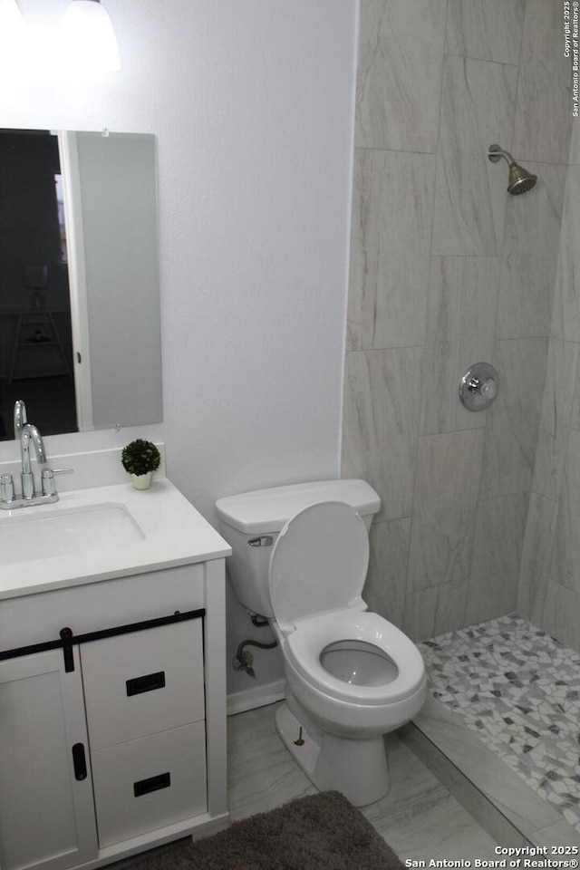 bathroom with tiled shower, vanity, and toilet