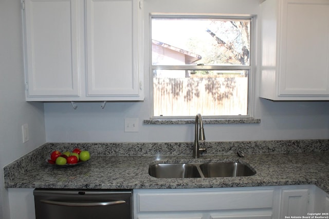 kitchen with stainless steel dishwasher, white cabinets, dark stone counters, and sink