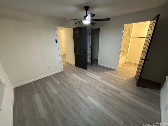 unfurnished bedroom with light wood-type flooring, ceiling fan, a walk in closet, and a closet