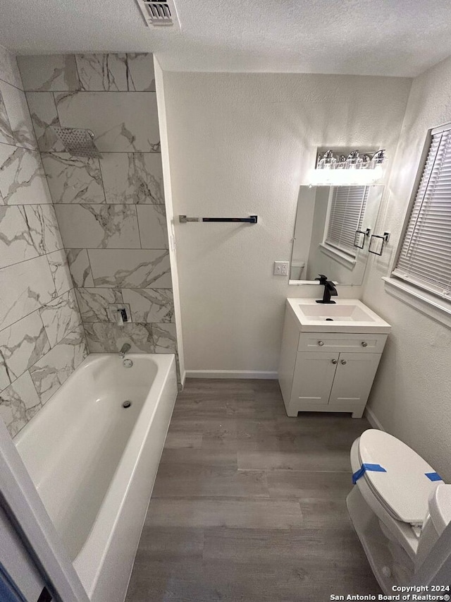 full bathroom featuring toilet, hardwood / wood-style flooring, tiled shower / bath, a textured ceiling, and vanity