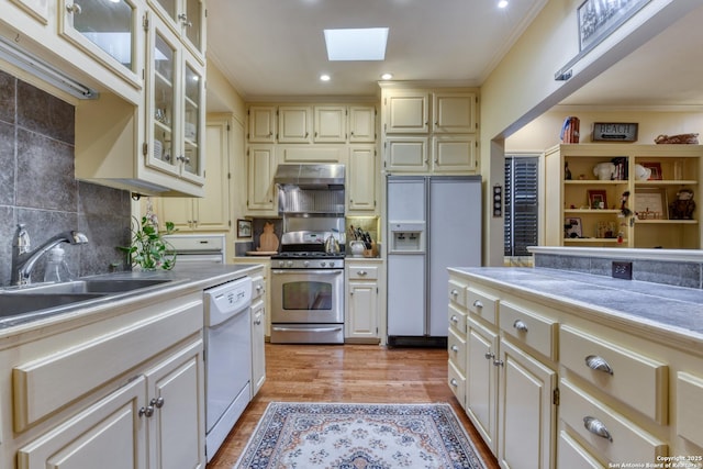 kitchen with sink, white appliances, a skylight, light hardwood / wood-style floors, and ornamental molding