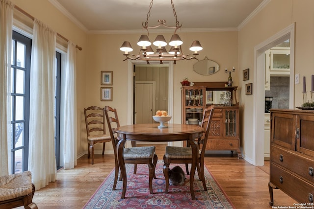 dining room featuring a tile fireplace, ornamental molding, a chandelier, and light wood-type flooring