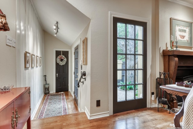 doorway to outside with a wealth of natural light, rail lighting, vaulted ceiling, and light wood-type flooring