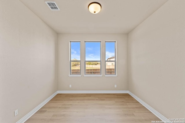 empty room featuring light wood-type flooring, visible vents, and baseboards