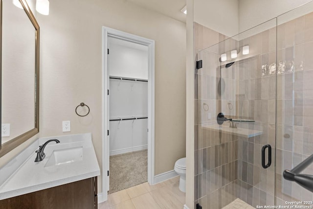 bathroom with a spacious closet, toilet, a stall shower, vanity, and baseboards