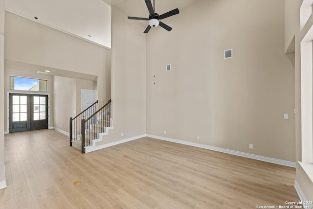 unfurnished living room featuring french doors, visible vents, stairway, light wood-style flooring, and a towering ceiling