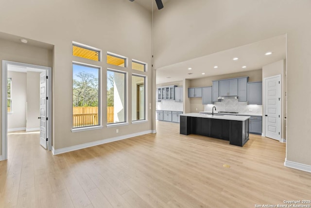 kitchen featuring light wood finished floors, an island with sink, light countertops, under cabinet range hood, and a sink