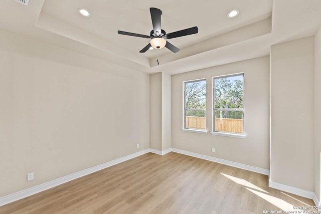 empty room featuring light wood-style floors, baseboards, a tray ceiling, and recessed lighting