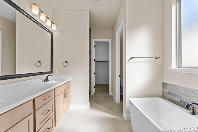 full bath with visible vents, tile patterned floors, a walk in closet, vanity, and a freestanding tub