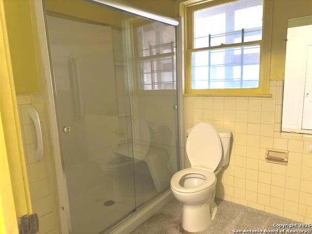 bathroom with toilet, tile walls, and a shower with door