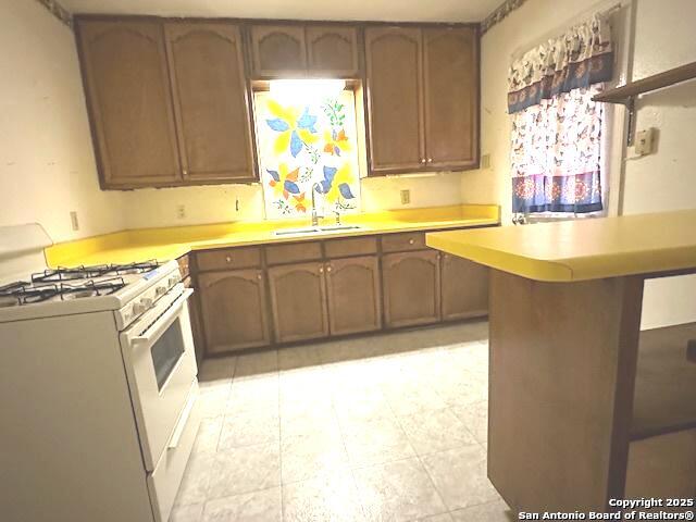 kitchen with white gas range, kitchen peninsula, and sink