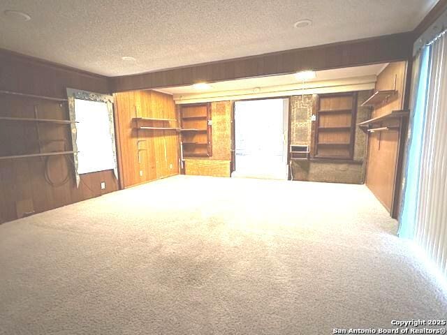 interior space featuring a textured ceiling, carpet, and wooden walls