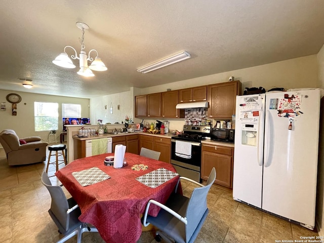 kitchen featuring decorative light fixtures, kitchen peninsula, an inviting chandelier, white appliances, and a textured ceiling