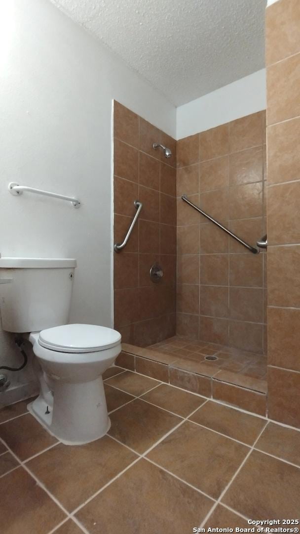 bathroom featuring toilet, tiled shower, tile patterned floors, and a textured ceiling