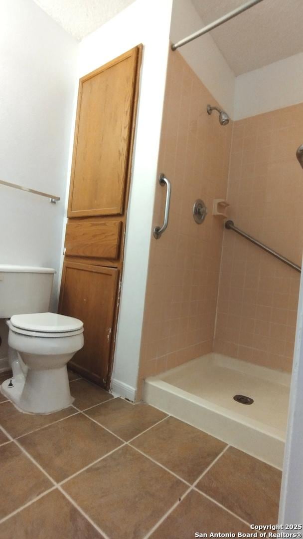 bathroom featuring toilet, tile patterned floors, and tiled shower