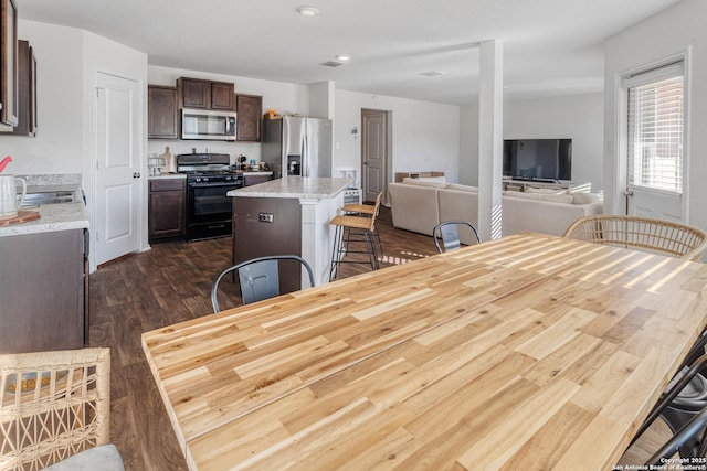 kitchen featuring a kitchen bar, appliances with stainless steel finishes, dark wood-type flooring, dark brown cabinets, and a kitchen island